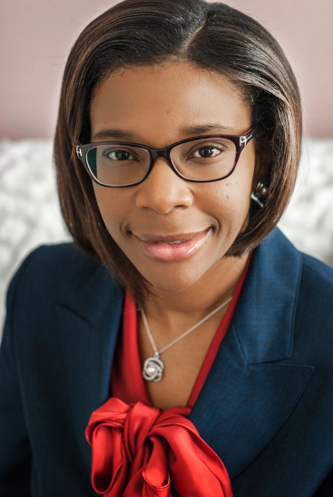 Professional woman wearing glasses and a blazer, smiling gently.